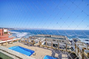 Ein Poolbereich mit Blick auf das Meer, ein Gebäude mit Flachdach und ein klarer Himmel.