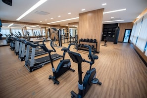 Uma academia com equipamentos de exercícios, piso de madeira e grandes janelas.