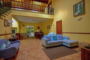 A spacious living area with a high ceiling, a dining table, a sofa, and a staircase leading to an upper level. - Apartment 3 at Casa da Avo Ines (São Brás)
