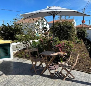 An outdoor patio with a table and chairs, an umbrella, and a garden with flowers and shrubs. - Apartment 2 at Casa da Avo Ines (São Brás)