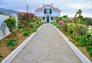 A house with a paved pathway leading to the entrance, surrounded by various plants and a garden. - Apartment 2 at Casa da Avo Ines (São Brás)