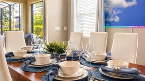 Een eettafel gedekt voor zes personen, met witte stoelen, blauwe placemats en transparant servies.
