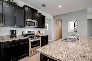 A modern kitchen with dark cabinets, stainless steel appliances, granite countertops, and a large mirror above the sink. - Near Disney & Epic 5BR w/ Pool & Game Room (Davenport)