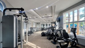Een sportschool met cardioapparatuur, krachtstations en een groot raam met uitzicht op palmbomen.