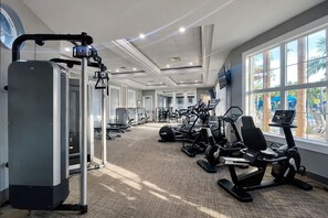 A gym with cardio machines, weight stations, and a large window with a view of palm trees. - Near Disney & Epic 5BR w/ Pool & Game Room (Davenport)