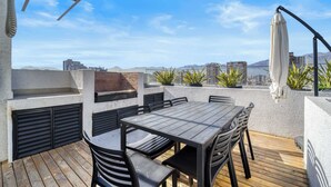 Um pátio externo com mesa e cadeiras de madeira, churrasqueira e plantas em vasos.