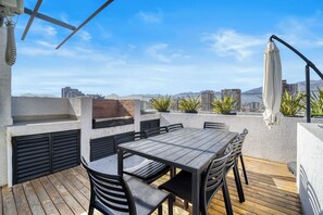 Eine Terrasse im Freien mit Holztisch und -stühlen, einem Grill und Kübelpflanzen.
