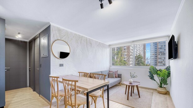 Sala moderna com mesa de jantar, cadeiras, sofá, janela grande com vista para edifícios e TV na parede.