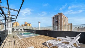 Terraço no telhado com piscina, espreguiçadeiras e vista para os edifícios ao redor.