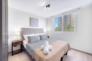 Ein Schlafzimmer mit einem Bett, einem Nachttisch, einem Fenster und Blick auf Gebäude.