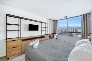 Ein modernes Hotelzimmer mit einem großen Bett, einem an der Wand montierten Fernseher, einem Schreibtisch und Blick auf die Stadt.