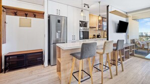 Et moderne køkken med en central ø, barstole, en indbygget bænk og et tv ophængt på væggen.