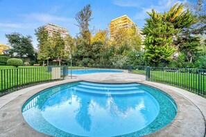 Ein runder Pool mit einer gefliesten Kante, umgeben von einem Metallzaun, Bäume im Hintergrund.