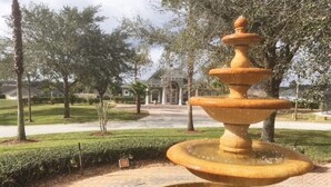 A fountain with multiple tiers in a landscaped area with trees and a building in the background. - Luxury 5 bedroom home with fantastic views pool and lanai. (Davenport)