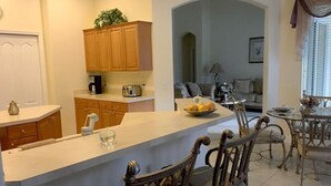 A kitchen with wooden cabinets, a white countertop, and a dining area with metal chairs and a glass table. - Luxury 5 bedroom home with fantastic views pool and lanai. (Davenport)