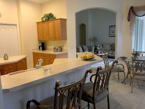 A kitchen with wooden cabinets, a white countertop, and a dining area with metal chairs and a glass table. - Luxury 5 bedroom home with fantastic views pool and lanai. (Davenport)