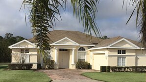 A two-story house with a front entrance, a driveway, and a well-maintained lawn. - Luxury 5 bedroom home with fantastic views pool and lanai. (Davenport)
