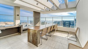 A modern office space with a large wooden desk, wicker chairs, and large windows offering city views.