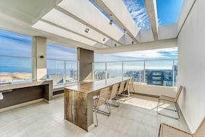 Un espace de bureau moderne doté d'un grand bureau en bois, de chaises en osier et de grandes fenêtres offrant une vue sur la ville.