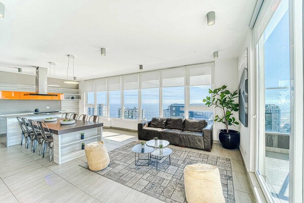 Un appartement moderne doté d’une cuisine, d’un coin repas, d’un salon et de grandes fenêtres offrant une vue sur la ville.