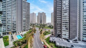 A high-rise residential building with multiple balconies, a swimming pool, and a road with cars.