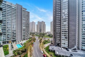 Un immeuble résidentiel de grande hauteur, doté de nombreux balcons, d’une piscine et situé près d’une route où circulent des voitures.