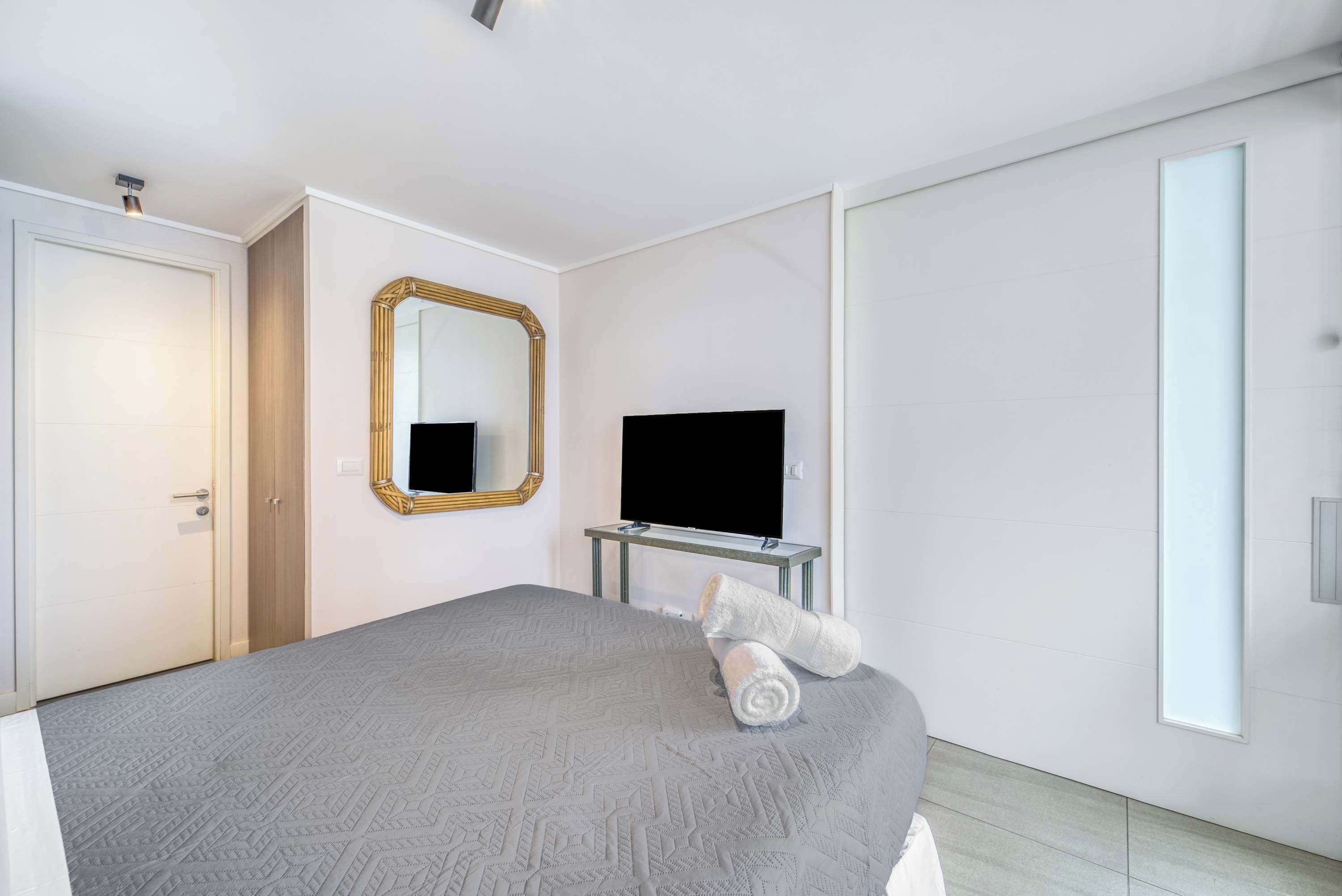 Ein modernes Hotelzimmer mit einem Bett, einem Fernseher, einem Spiegel und einer Schiebetür.