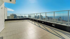 A rooftop terrace with a city view, glass railings, and a tiled floor.