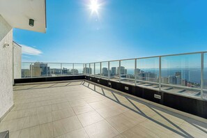 A rooftop terrace with a city view, glass railings, and a tiled floor.