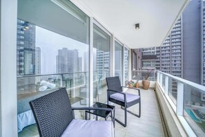 Un balcon avec des garde-corps en verre, un lit, deux chaises et une petite table.