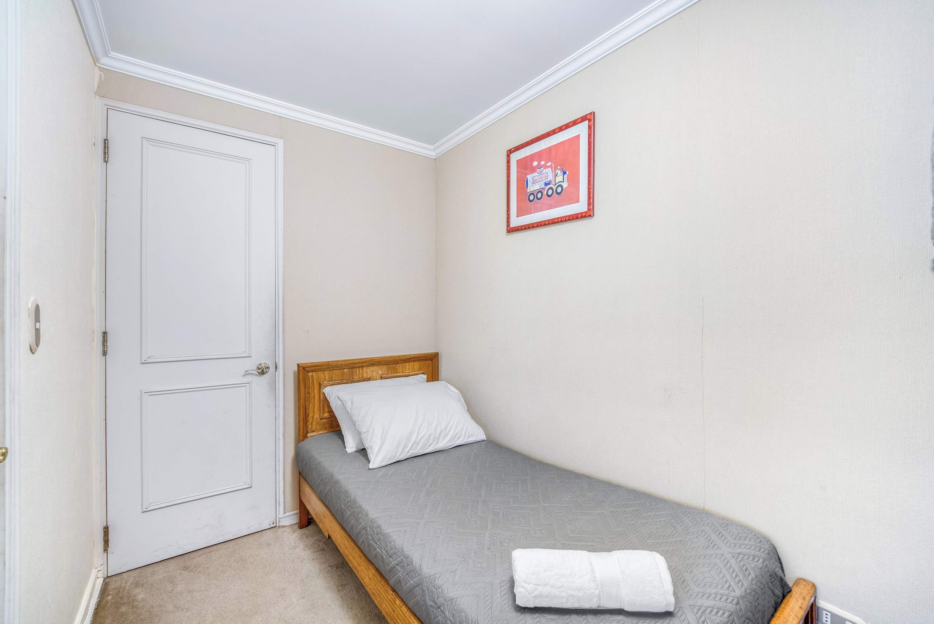 Un lit simple avec une couverture grise, une porte blanche et un tableau encadré accroché au mur.
