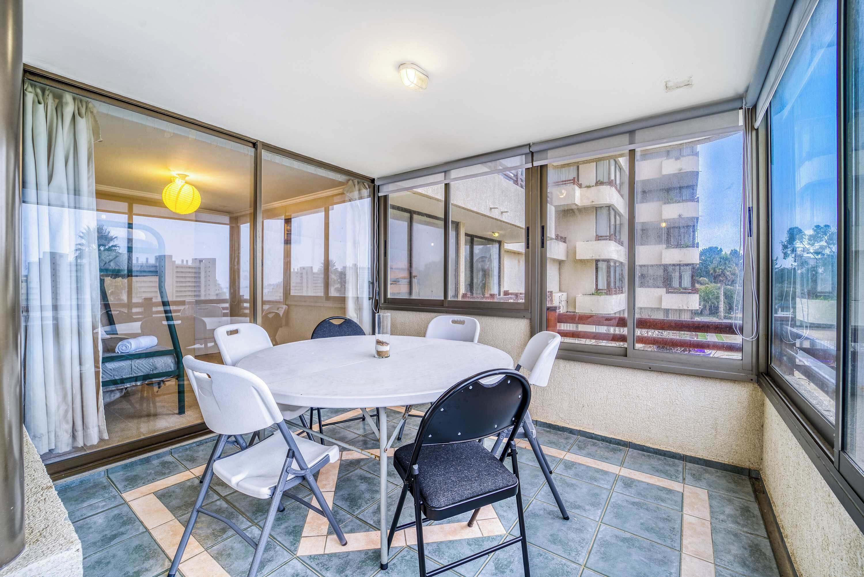Une pièce avec une table ronde et des chaises, de grandes fenêtres et une vue sur des immeubles.