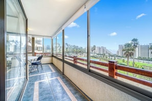 A balcony with a view of a cityscape, a table, and chairs.