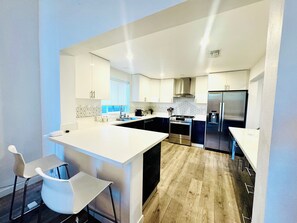 A modern kitchen with white cabinetry, a central island, stainless steel appliances, and a wooden floor. - Perfect 4-bedroom house with AC & High ceilings for the Summer (Los Angeles)