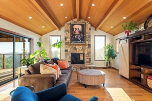 A spacious living room with a stone fireplace, a sofa, an ottoman, and a television.