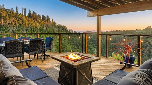 A deck with outdoor furniture, a fire pit, and a view of a forested hillside.