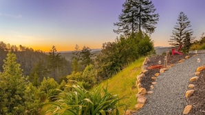 A scenic outdoor area with a gravel path, surrounded by greenery and trees, leading to a viewpoint overlooking a forested valley.
