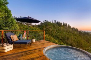 A wooden deck with a hot tub, a lounge chair, and a table with a person.