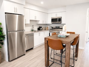 Une cuisine moderne dotée d’appareils électroménagers en acier inoxydable, de meubles blancs et d’une table à manger en bois avec des chaises.