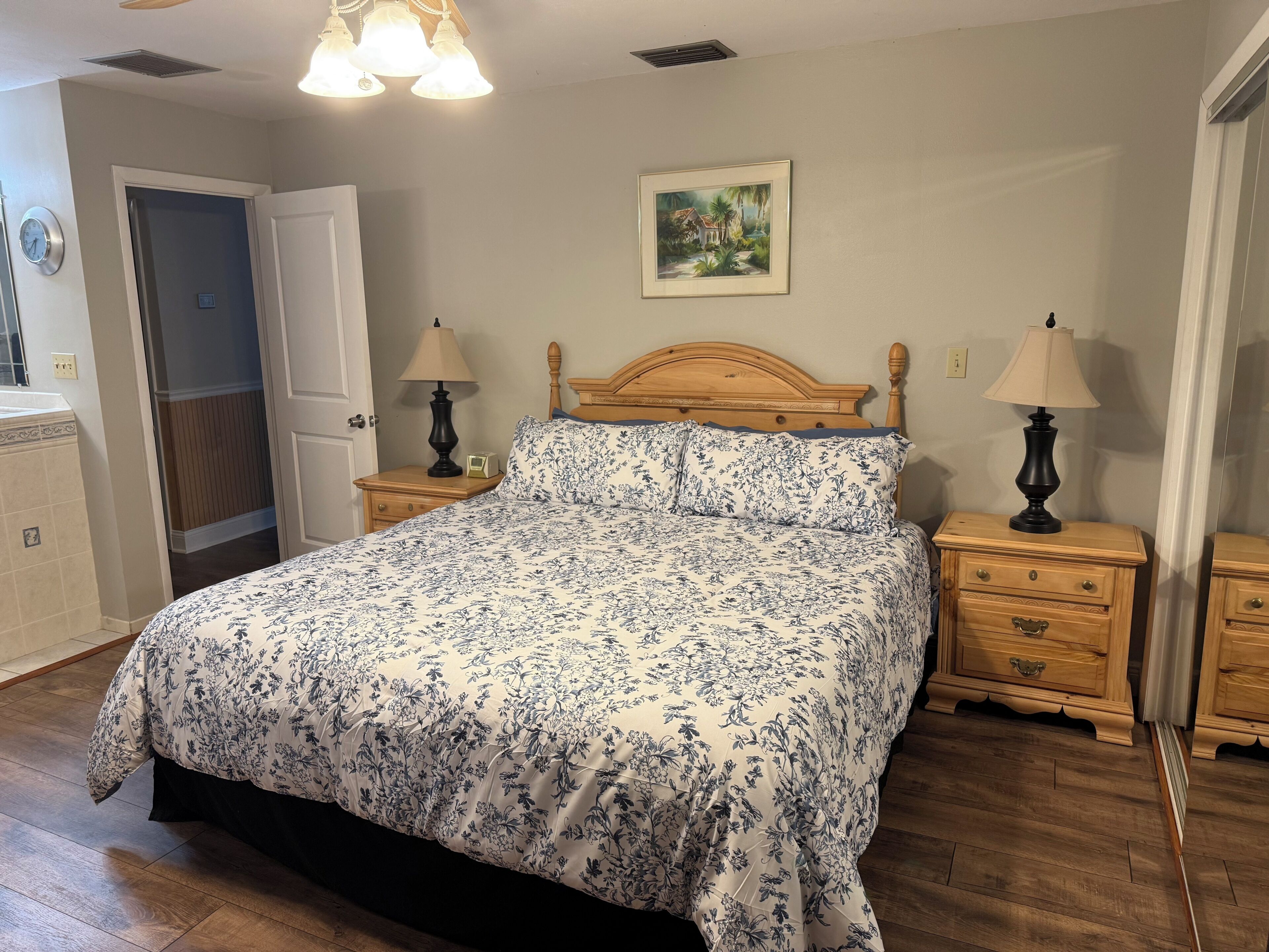 A bedroom with a wooden bed, two bedside tables with lamps, a door, and a painting on the wall.
