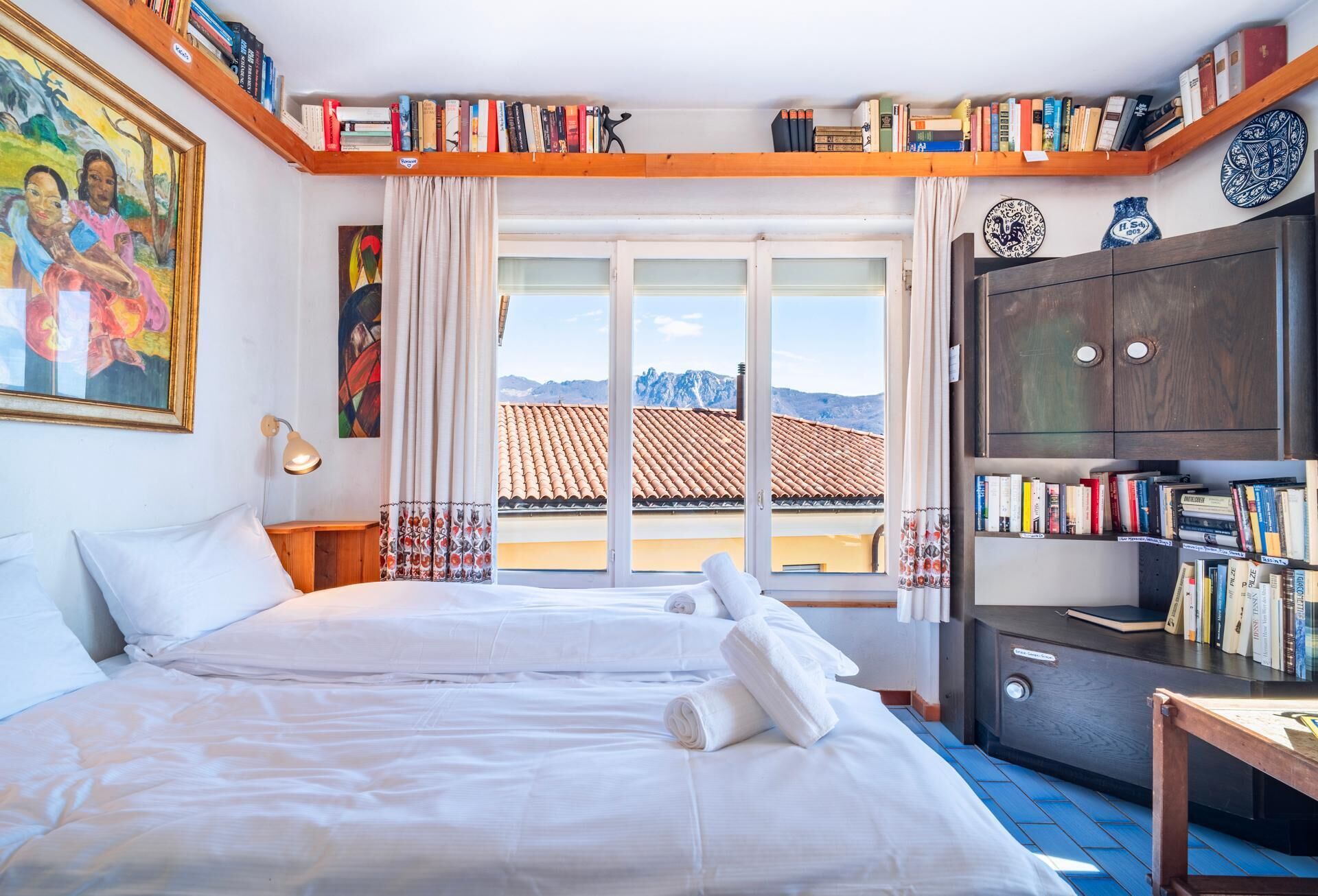 Ein Hotelzimmer mit Bett, Schreibtisch, Bücherregal und Blick auf die Berge.