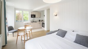 Una camera da letto moderna con un letto grande, un'area pranzo con tavolo e sedie, un angolo cottura con elettrodomestici e vista su spazi verdi.