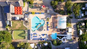 An aerial view of a resort with a swimming pool, sun loungers, a tennis court, and a water slide.