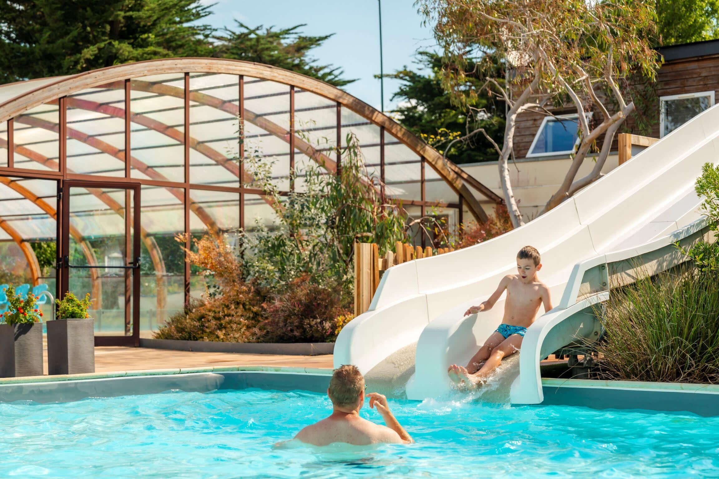 A pool with a slide, a greenhouse structure, and a person in the water.