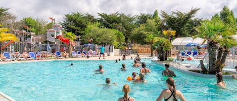 Una piscina con gente, sillas de descanso y palmeras.