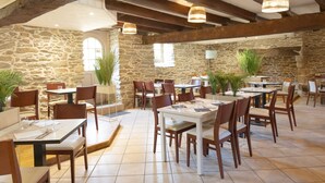 Ein Restaurant mit Steinwänden, Holzbalken und mehreren Tischen und Stühlen.