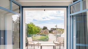 Ein Balkon mit zwei Stühlen und einer Bank, ein freier Blick auf einen grünen Garten und eine Straße im Hintergrund.