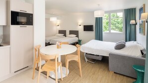 A compact hotel room with a kitchenette, a dining area, a bed, and a sofa. - Logis - Grand Privilège - 4p (Sarzeau)