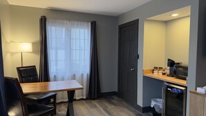 Une chambre d’hôtel équipée d’une table à manger, de chaises, d’une lampe, d’une porte, d’un coin cuisine et d’une fenêtre avec des rideaux.