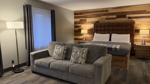 Une chambre d’hôtel avec un canapé, un lit doté d’une tête de lit en bois, une table de chevet et une lampe sur pied.